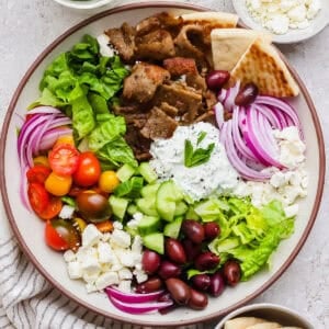 A bowl of chopped gyro salad with gyro meat, olives, feta, tomatoes, red onion and tzatziki dressing.