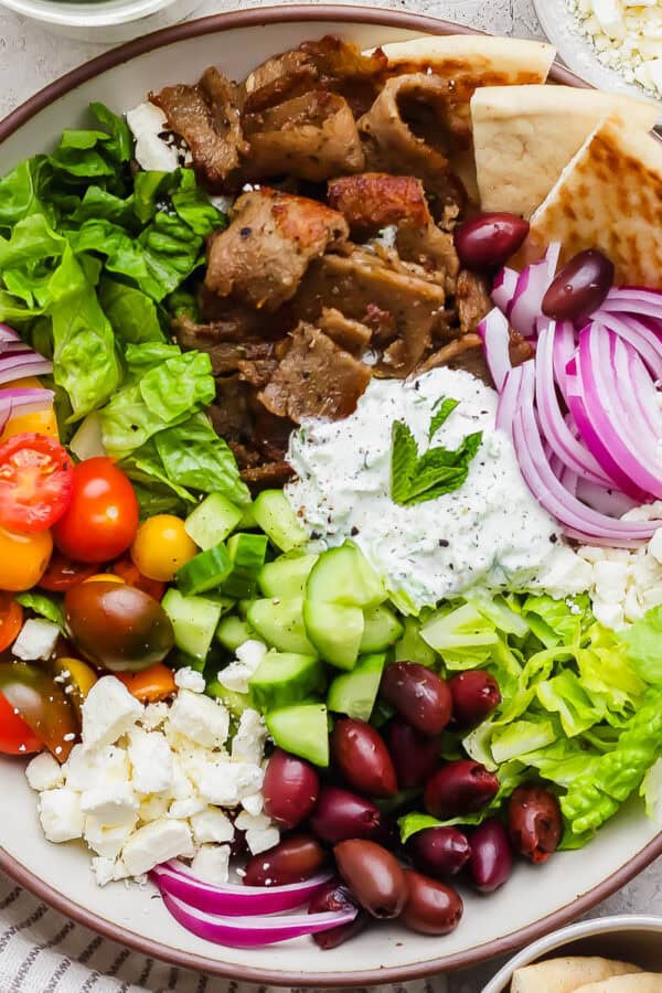 A bowl of chopped gyro salad with gyro meat, olives, feta, tomatoes, red onion and tzatziki dressing.