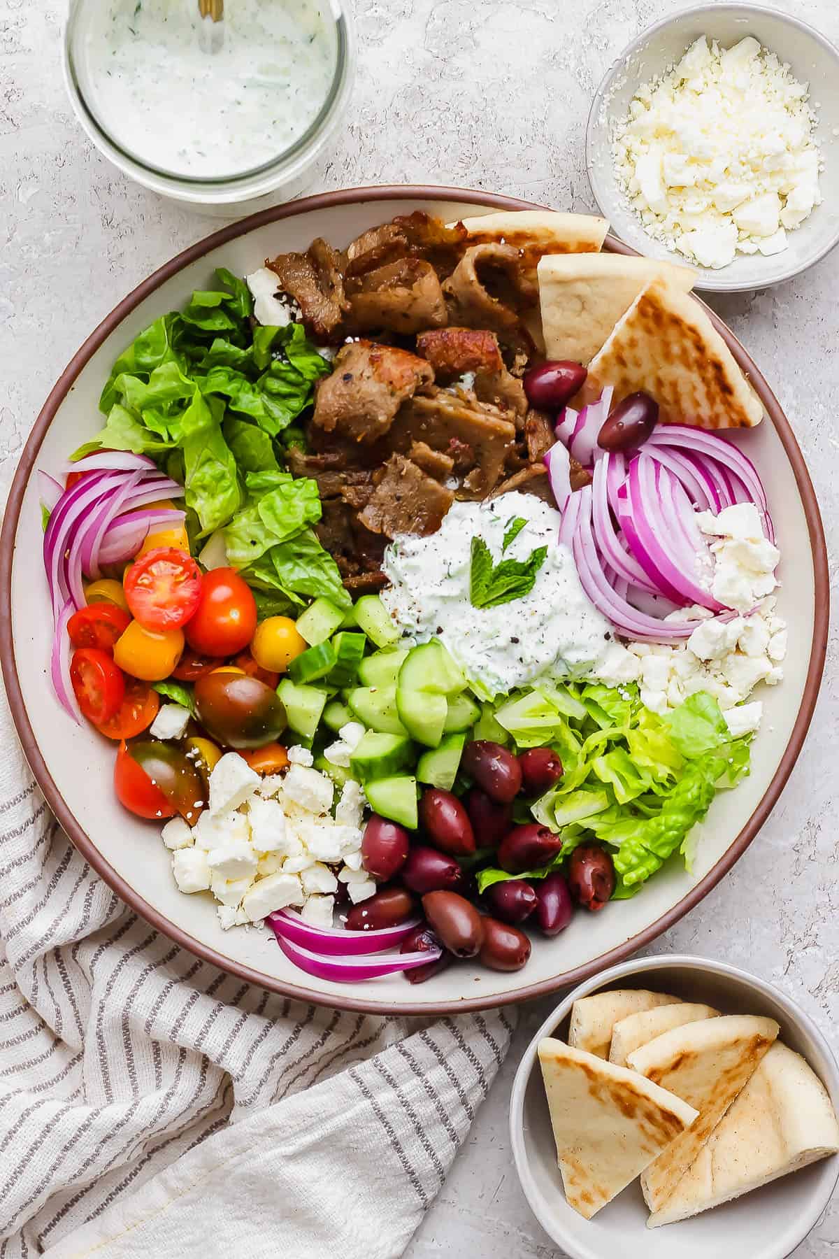 Gyro salad in a bowl garnished with feta cheese and tzatziki dressing.