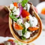 Someone holding a gyro smash burger taco with tzatziki sauce and fresh dill.