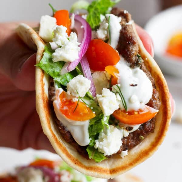 Someone holding a gyro smash burger taco with tzatziki sauce and fresh dill.