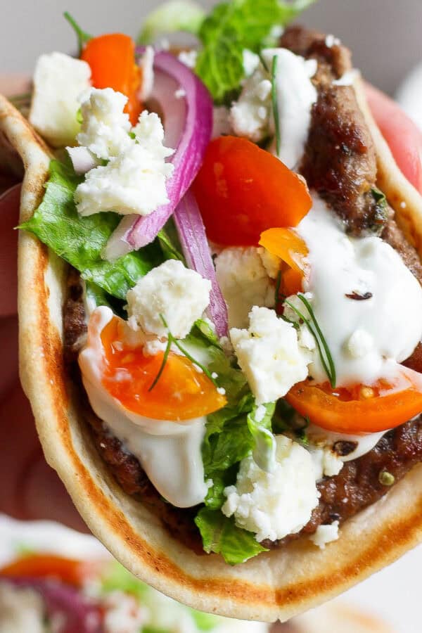 Someone holding a gyro smash burger taco with tzatziki sauce and fresh dill.
