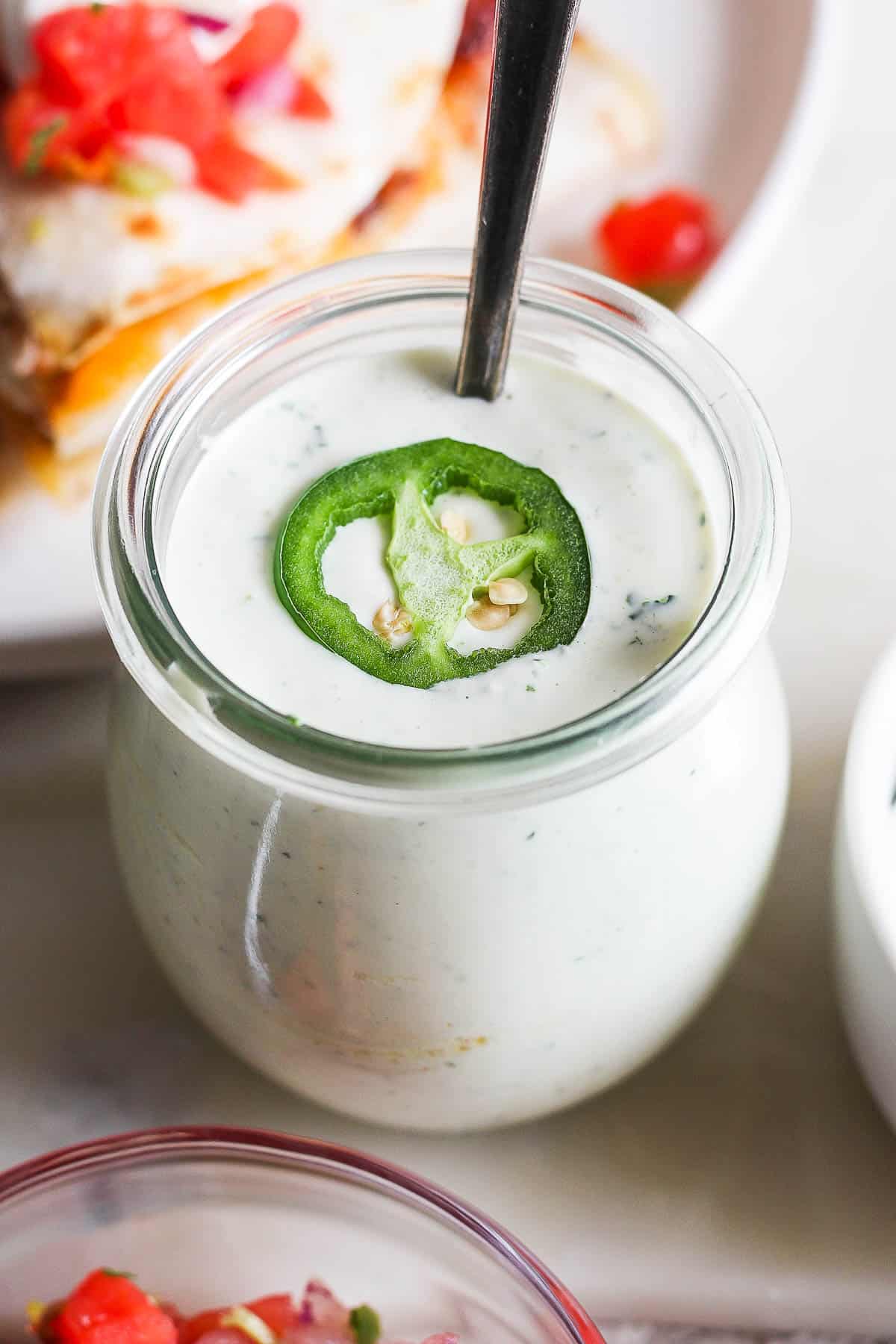 Jalapeno ranch in a small jar with a slice of jalapeno on the top.