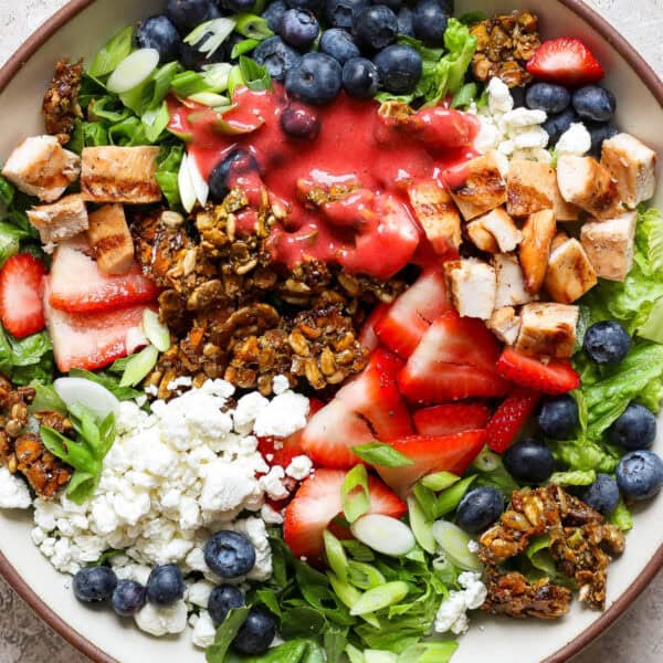 A bowl of seedy protein salad with strawberries, goat cheese, blueberries and granola.