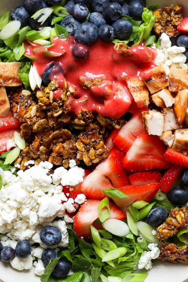 A bowl of seedy protein salad with strawberries, goat cheese, blueberries and granola.