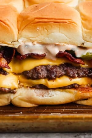Smash burger sliders on a baking sheet with burger sauce, melted cheese, bacon and pickles.