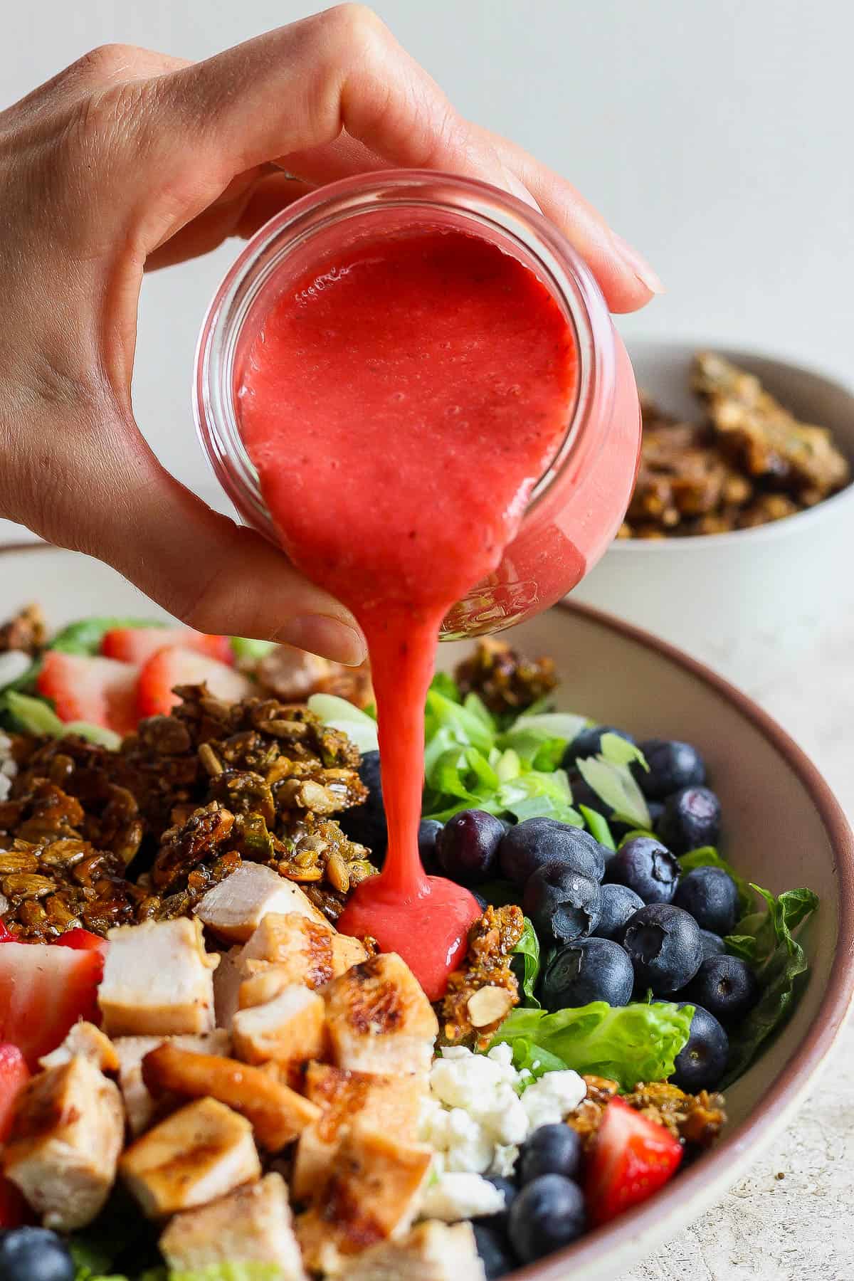 A jar of the strawberry vinaigrette being poured on the salad.