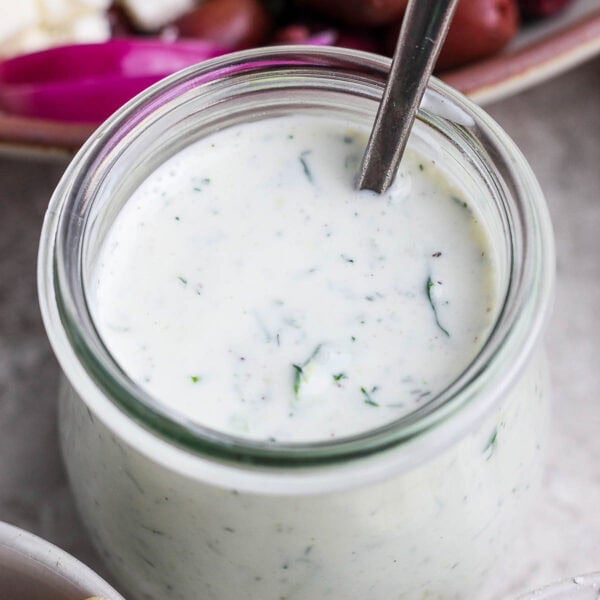 A jar of homemade tzatziki dressing with a spoon sticking out.