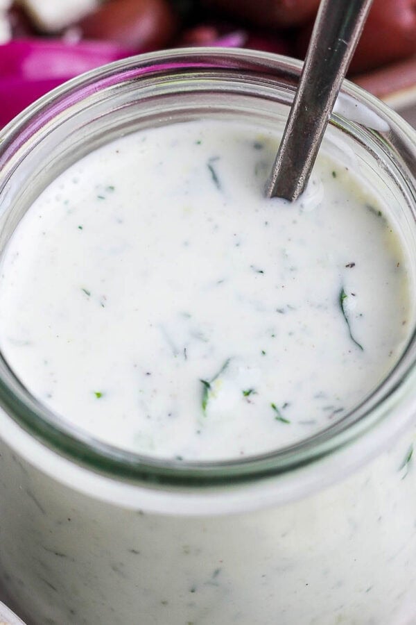 A jar of homemade tzatziki dressing with a spoon sticking out.