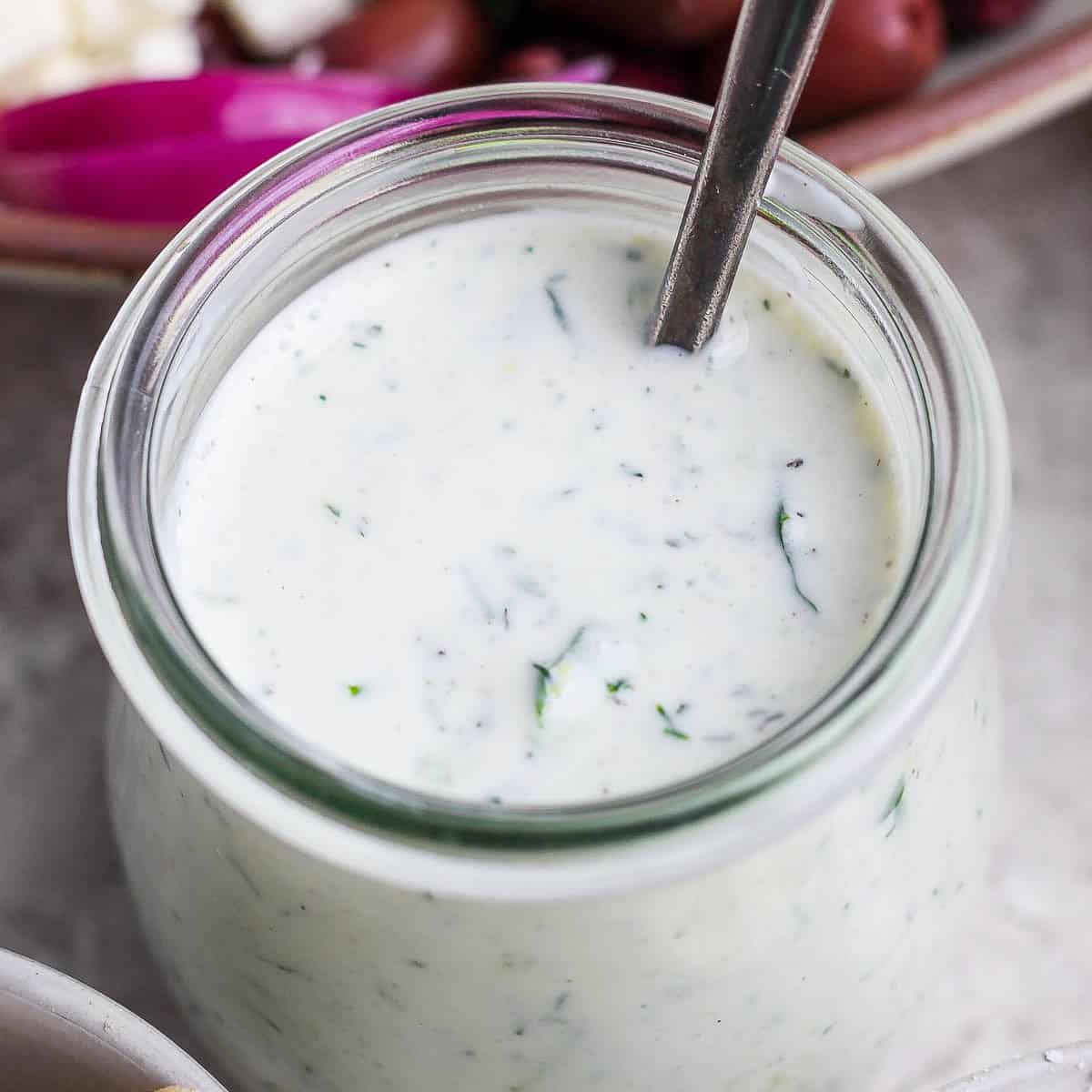 A jar of homemade tzatziki dressing with a spoon sticking out.