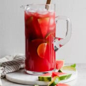 A pitcher of watermelon margaritas with ice, limes and watermelon slices inside and a spoon sticking out.
