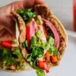 Someone holding a bahn mi smash burger taco with pickled veggies, sriracha mayo and cilantro.