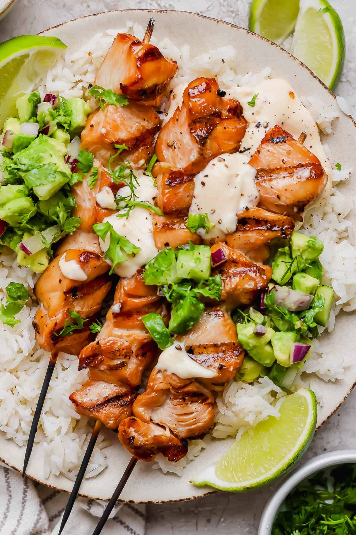 Bang bang chicken skewers over a bed of rice topped with cilantro and avocado salsa and bang bang sauce.