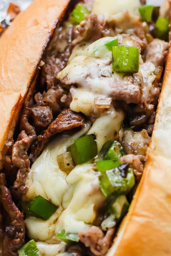A cheesy blackstone philly cheesesteak in a bun with green peppers.