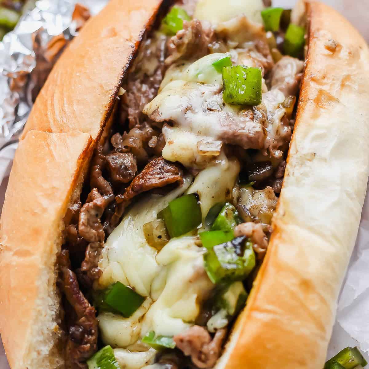 A cheesy blackstone philly cheesesteak in a bun with green peppers.
