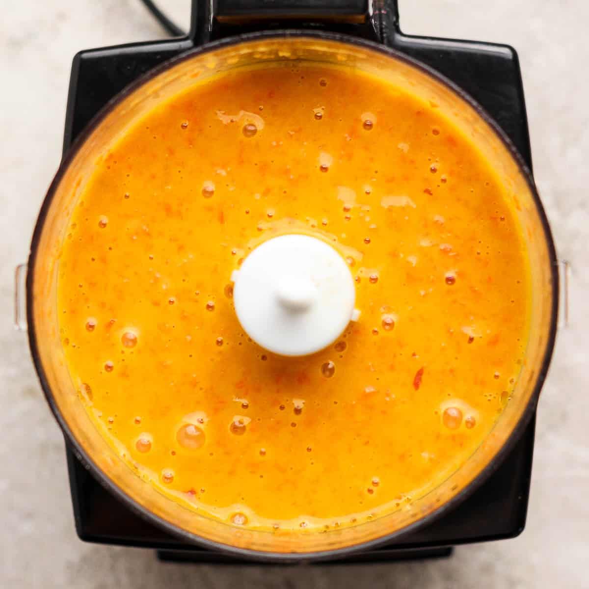 A top down shot of a small food processor filled with homemade carrot ginger salad dressing.
