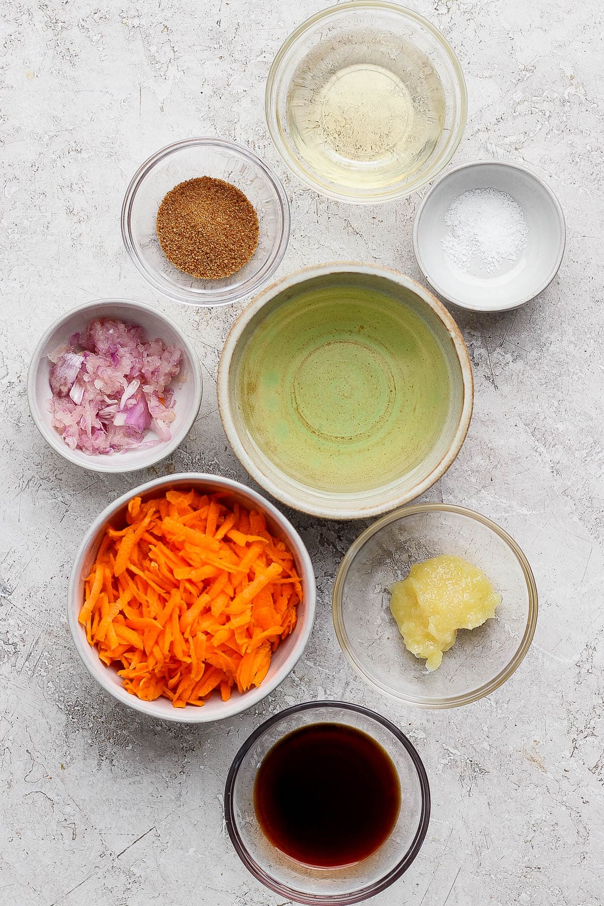 Individual bowls of rice vinegar, salt, olive oil, minced shallots, grated carrots, ginger paste, soy sauce, and grated carrots.