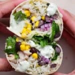 Someone holding a cilantro lime chicken burrito that has been cut in half showing the insides with corn, cilantro and black beans.