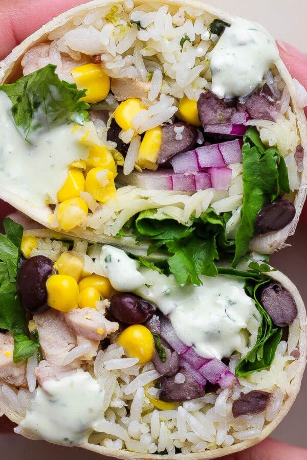 Someone holding a cilantro lime chicken burrito that has been cut in half showing the insides with corn, cilantro and black beans.