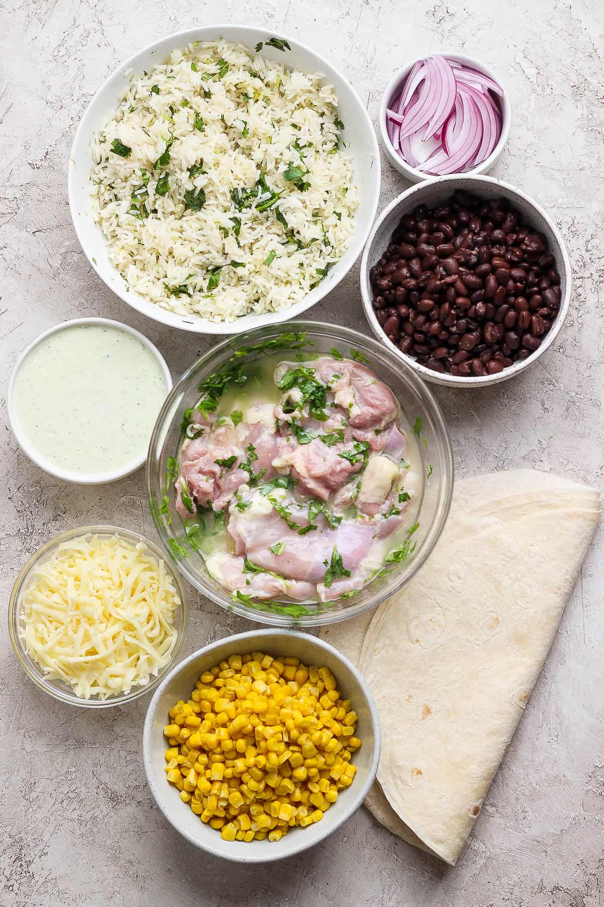 Ingredients for cilantro lime chicken burritos in separate bowls.