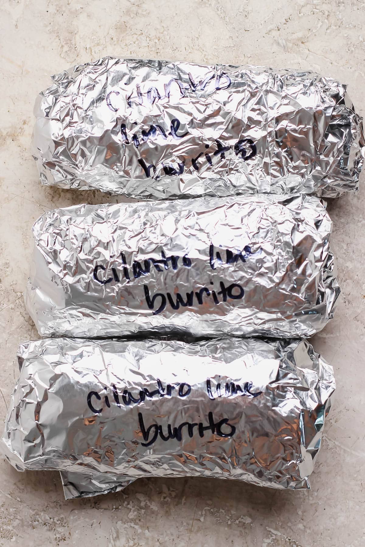 Three burritos individually wrapped in aluminum foil.