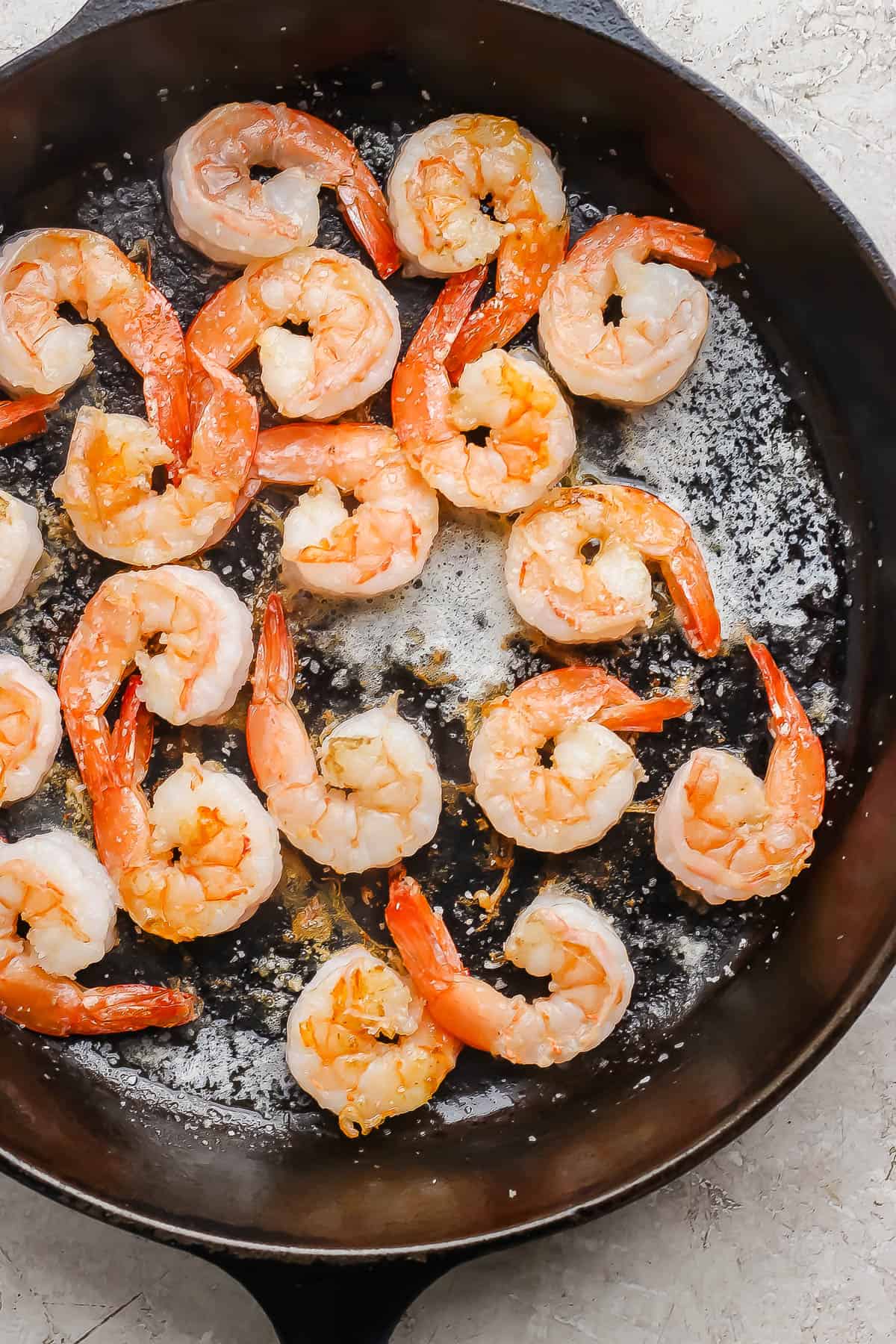 Shrimp being cooked in a cast-iron skillet with butter and salt.