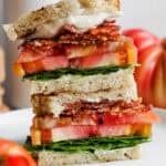 A stacked grilled blt on a plate with tomatoes next to it.