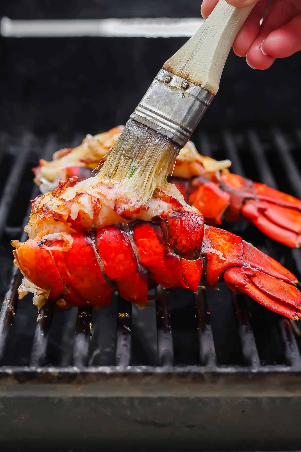 Lobster tails on the grill and being brushed with butter.