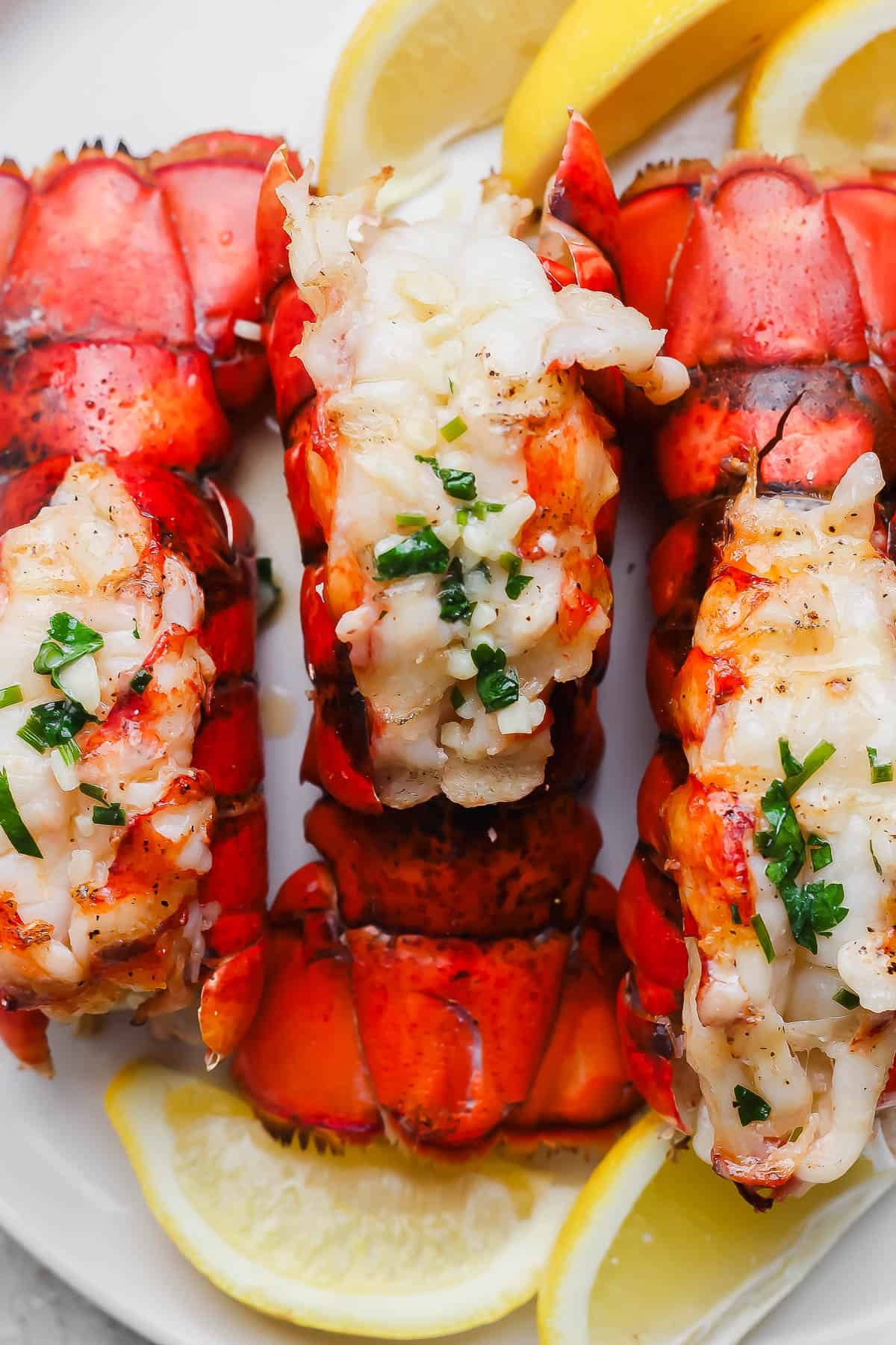 Three grilled lobster tails on a white plate.