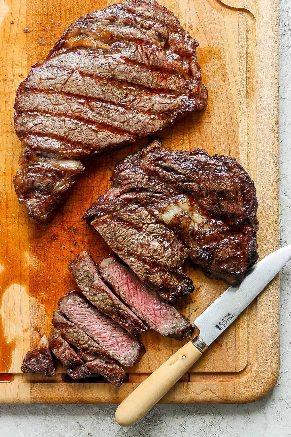 Sliced ribeye steak on a cutting board with a knife.