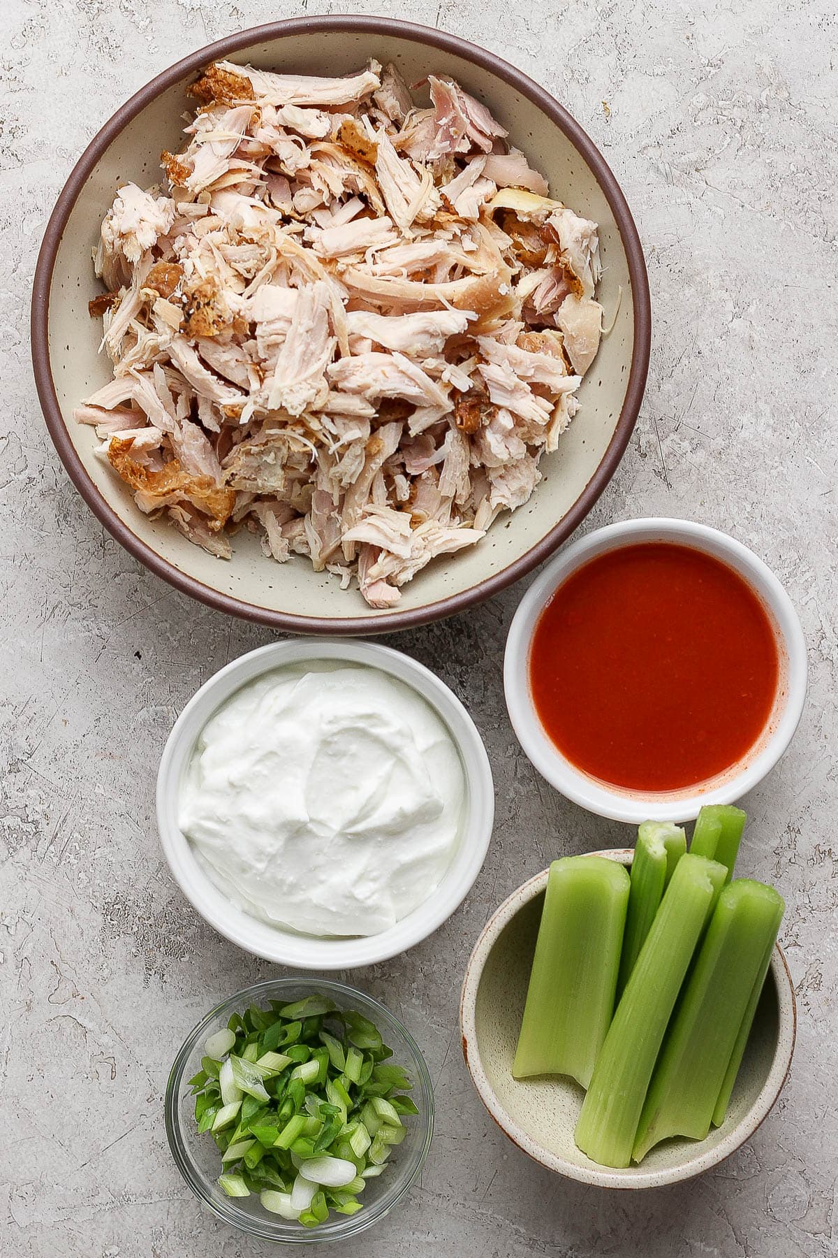 Individual bowls of shredded chicken, blended cottage cheese, celery sticks, Frank's red hot, and sliced green onions.