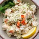 A bowl of lobster salad with fresh herbs and lemon wedges.
