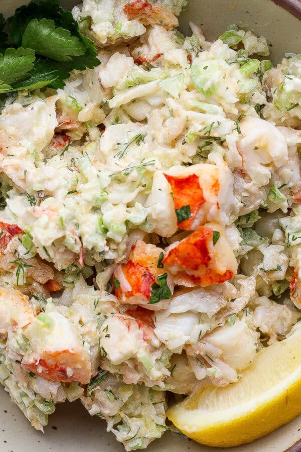 A bowl of lobster salad with fresh herbs and lemon wedges.