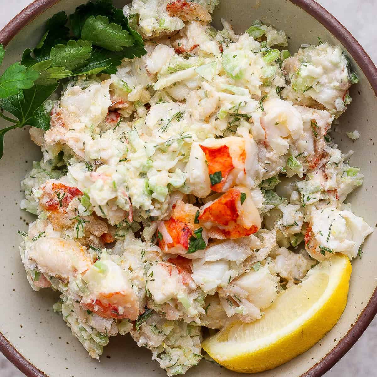 A bowl of lobster salad with fresh herbs and lemon wedges.
