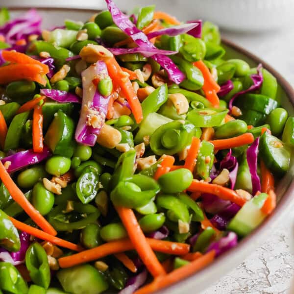 A bowl filled with a chopped pea salad with carrots, edamame, cabbage and chopped peanuts.