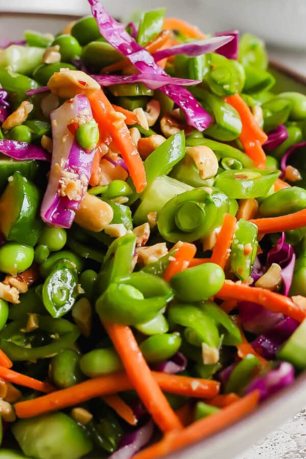 A bowl filled with a chopped pea salad with carrots, edamame, cabbage and chopped peanuts.