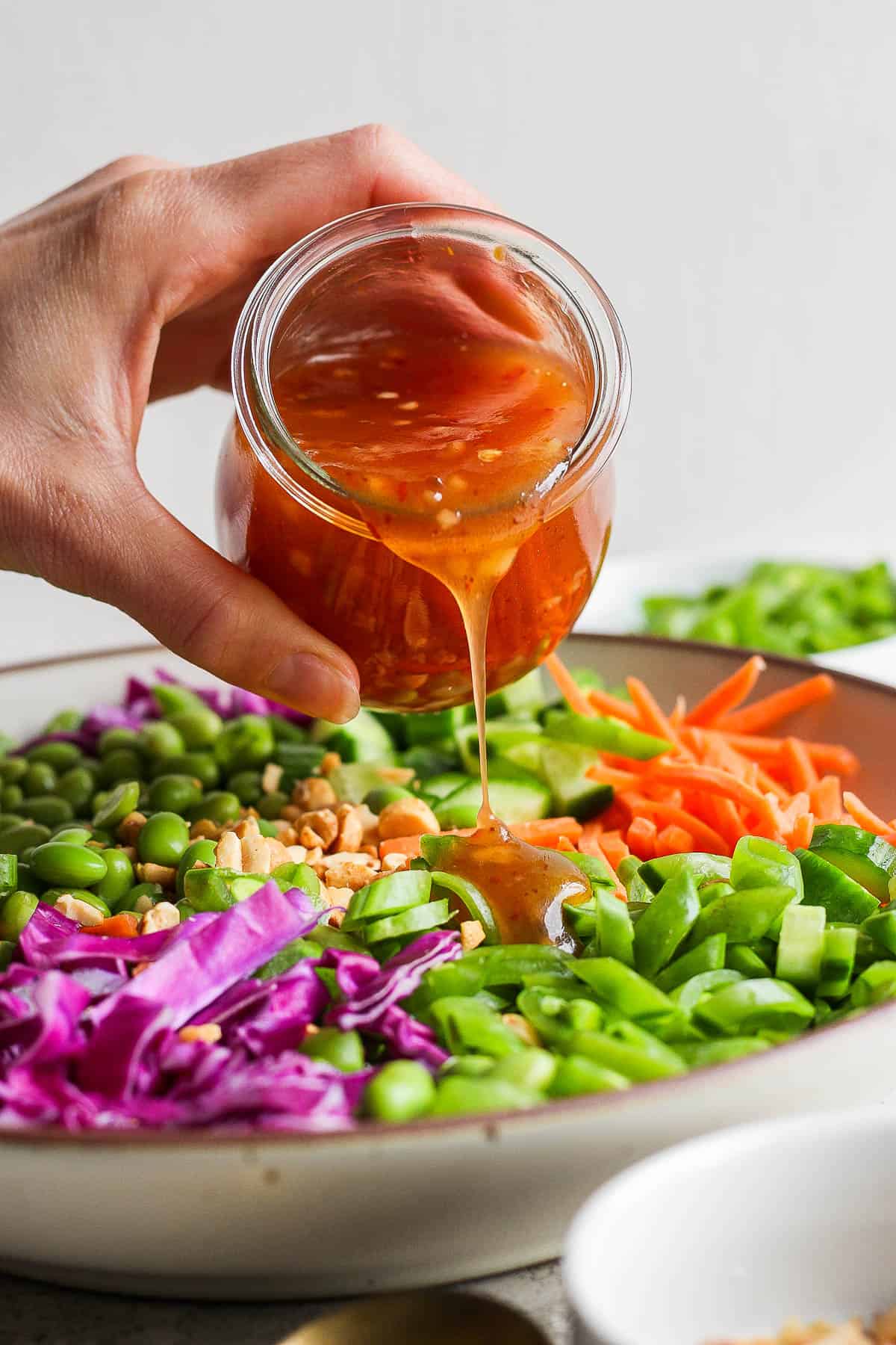 A jar of sweet chili vinaigrette being poured over a bowl of pea salad.