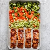 A sheet pan full of four salmon fillets, celery, carrots, and broccoli.