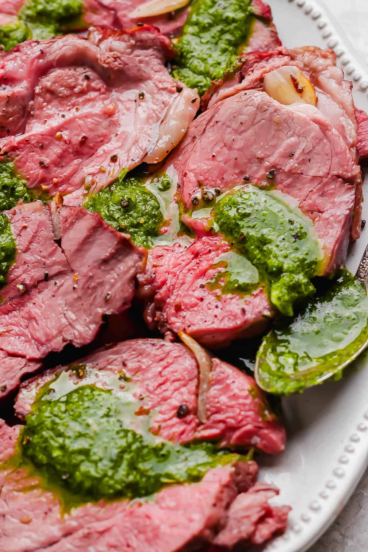 Sliced pieces of smoked lamb on a plater with chimichurri sauce.