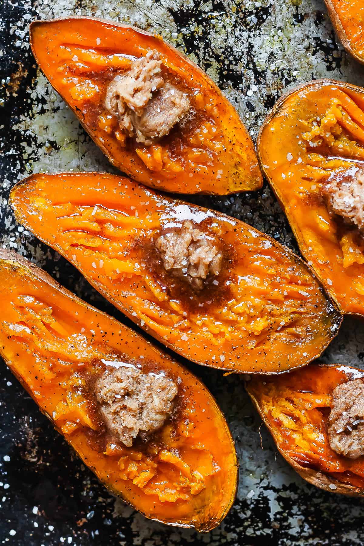 Smoked sweet potatoes on a baking sheet with a dollop of brown sugar and a sprinkling of sea salt on the top.