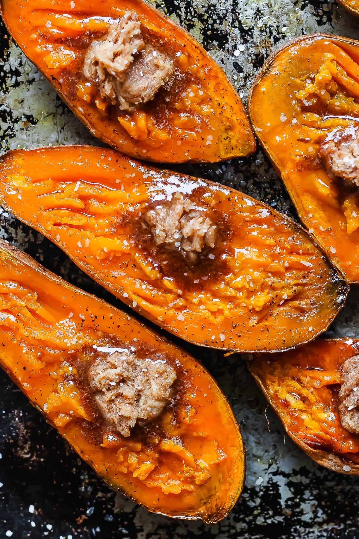 Smoked sweet potatoes on a baking sheet with a dollop of brown sugar and a sprinkling of sea salt on the top.