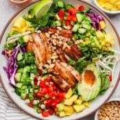 A bowl of chicken spring roll salad with avocado, red pepper, mango and sweet chili sauce with crushed peanuts.