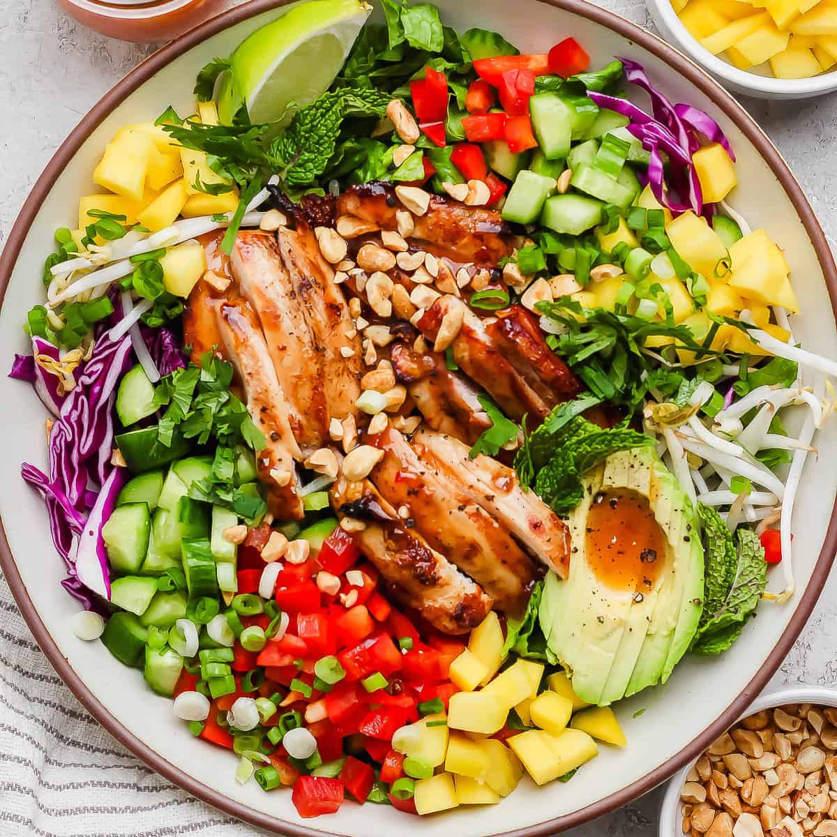 A bowl of chicken spring roll salad with avocado, red pepper, mango and sweet chili sauce with crushed peanuts.