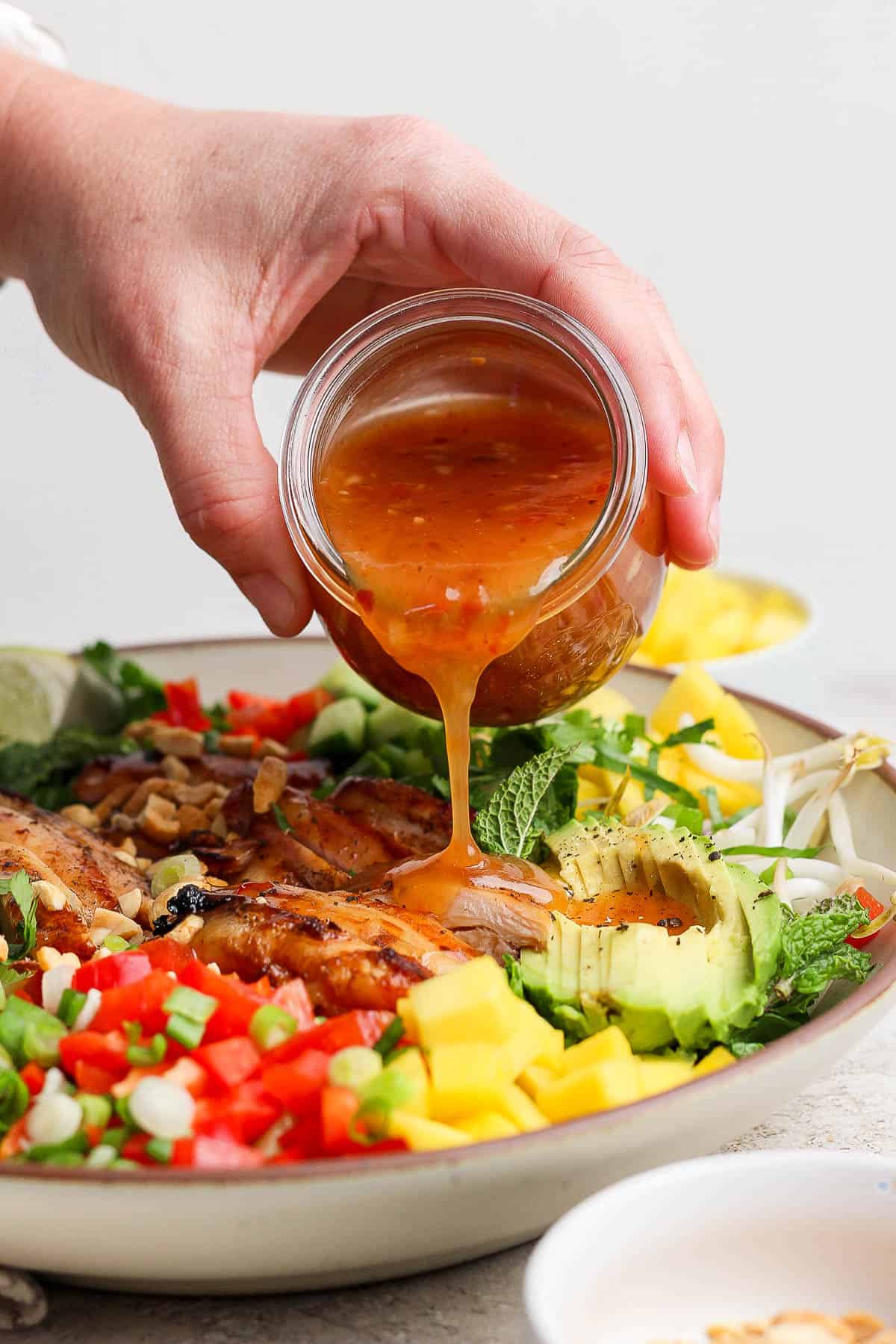 A hand pouring the dressing over a fully assembled salad.