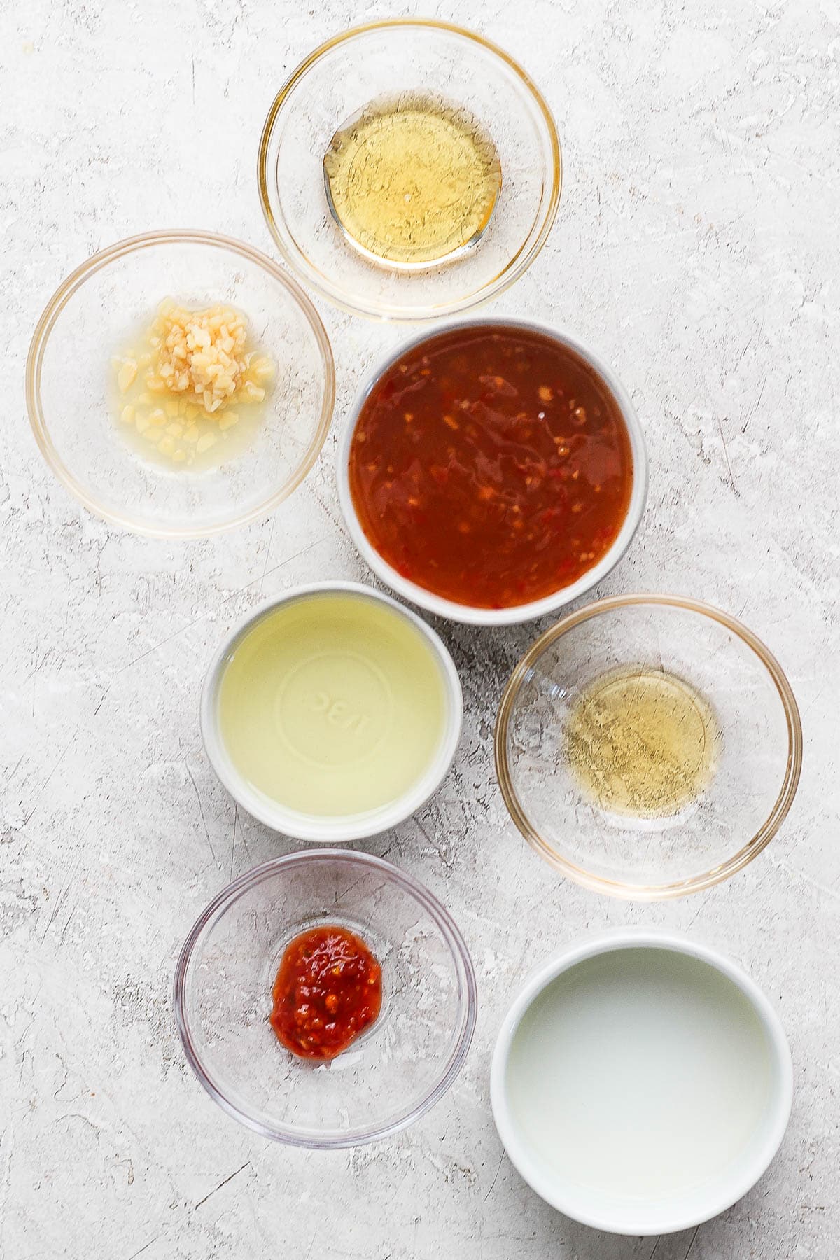 Individual bowls of honey, minced garlic, sweet chili sauce, olive oil, rice vinegar, sesame oi, and garlic chili sauce.
