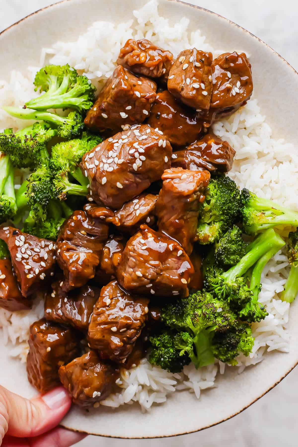 Teriyaki steak bites on a plate with rice and broccoli.