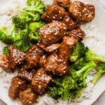 A plate of rice with roasted broccoli and teriyaki steak bites on top with sesame seeds.