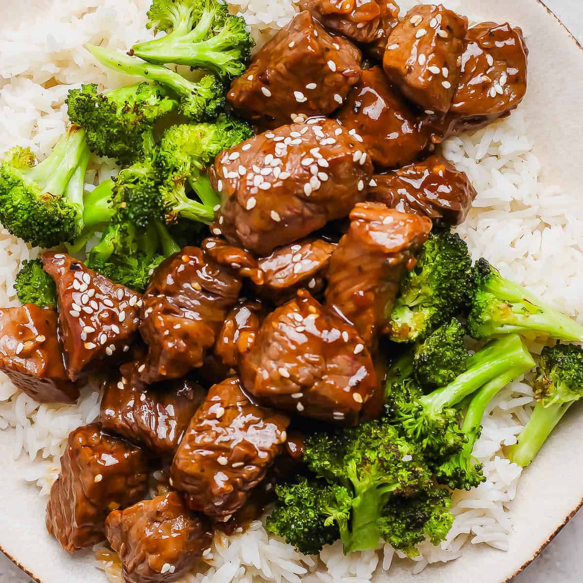 A plate of rice with roasted broccoli and teriyaki steak bites on top with sesame seeds.