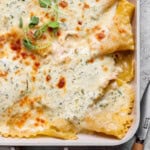 A close up of the corner of a sheet pan with chicken alfredo lasagna in it.