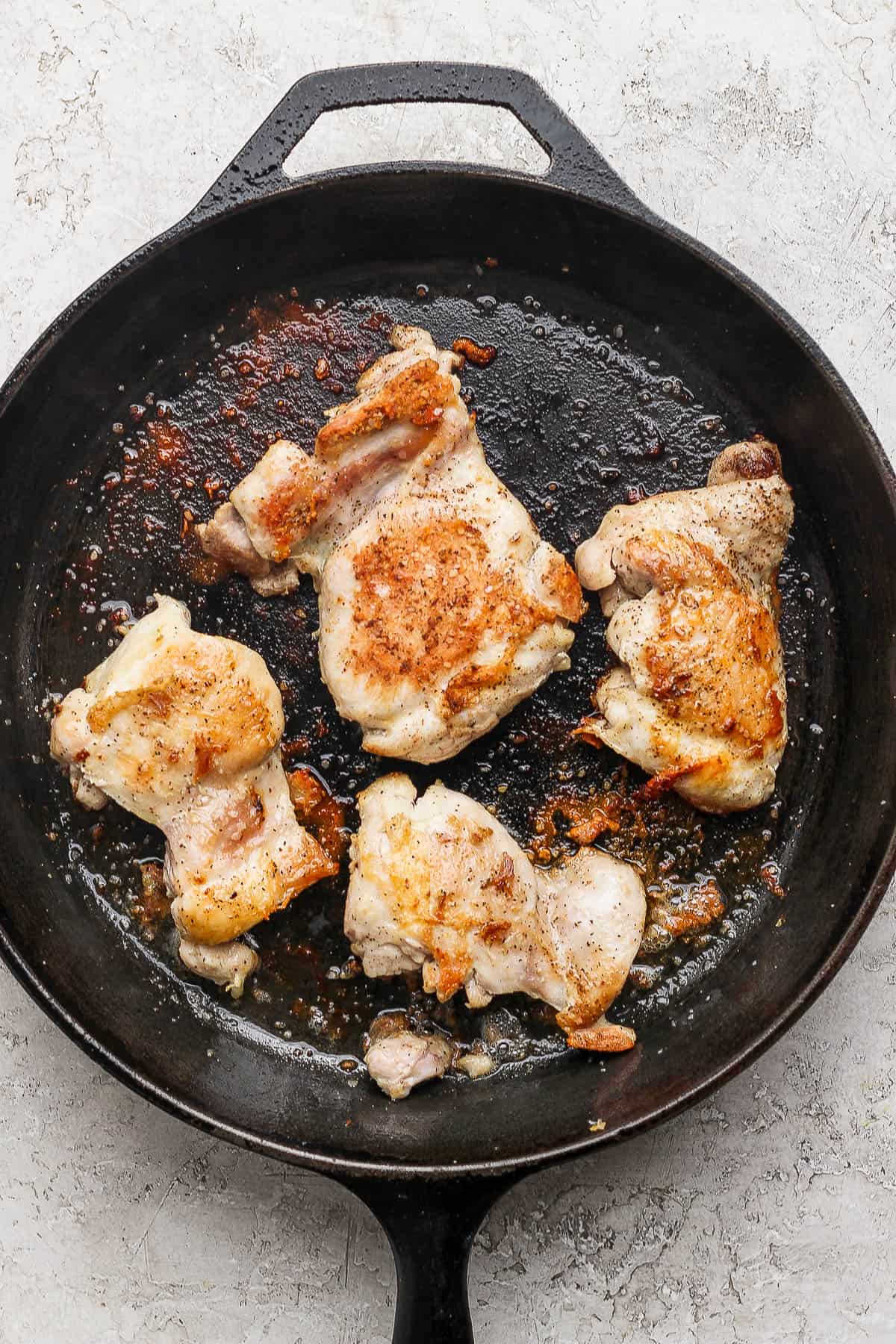Four chicken thighs cooking in a cast iron skillet.